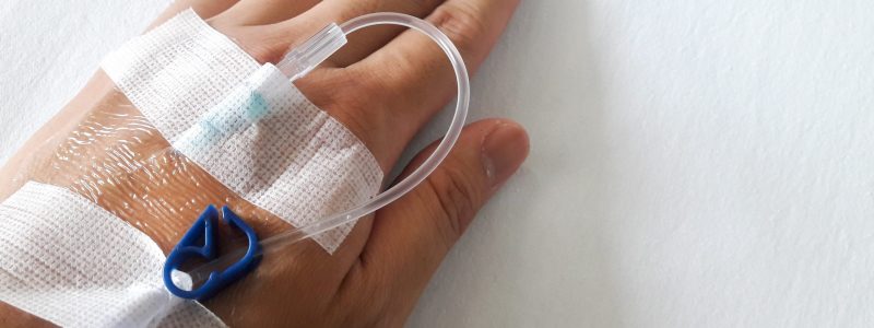 Patient hand with the tube of normal saline infusion on white cloth background